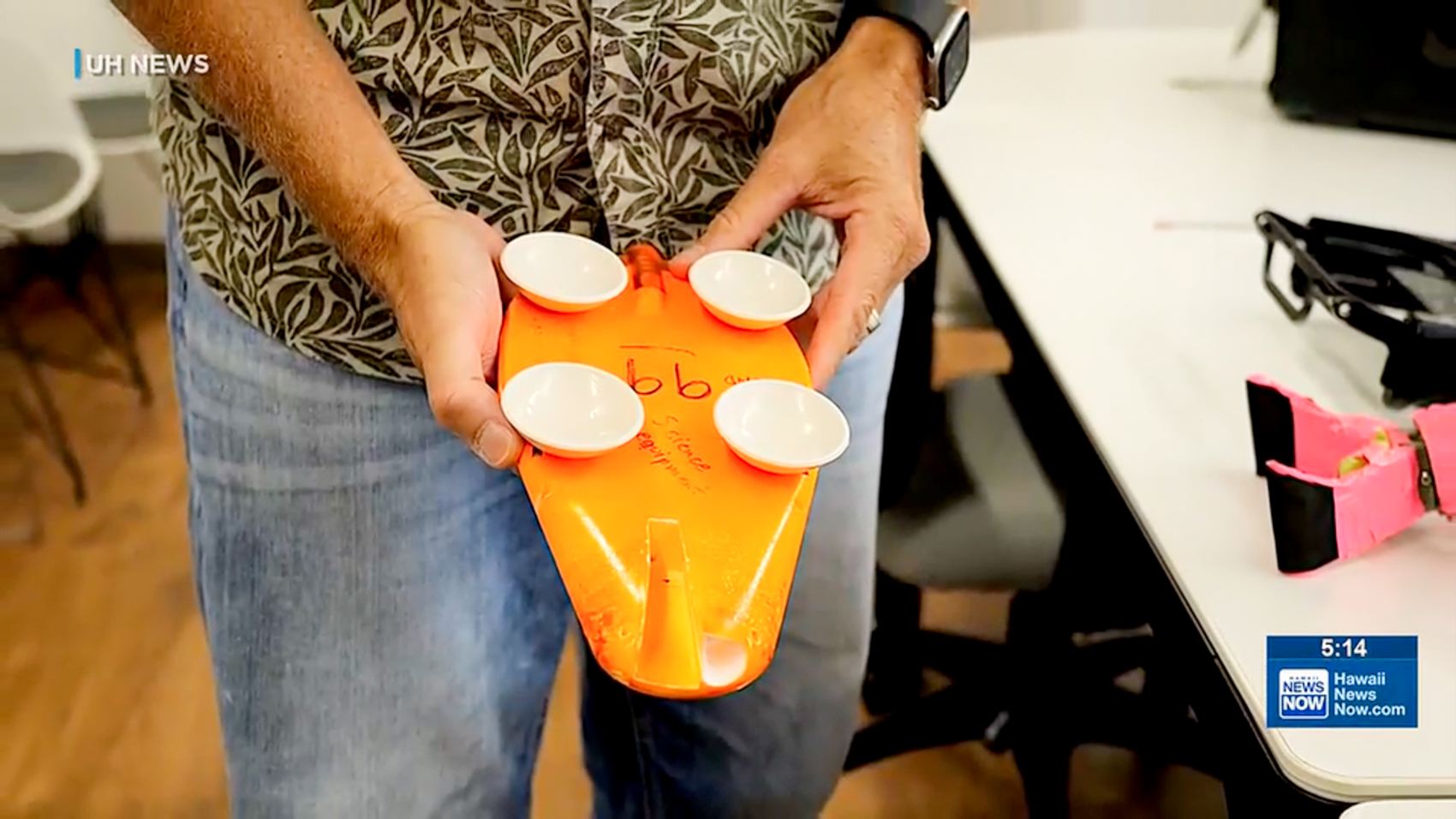 A researcher holds an orange CATS biologging tag with four white suction cups on its underside, marked in handwriting as science equipment.