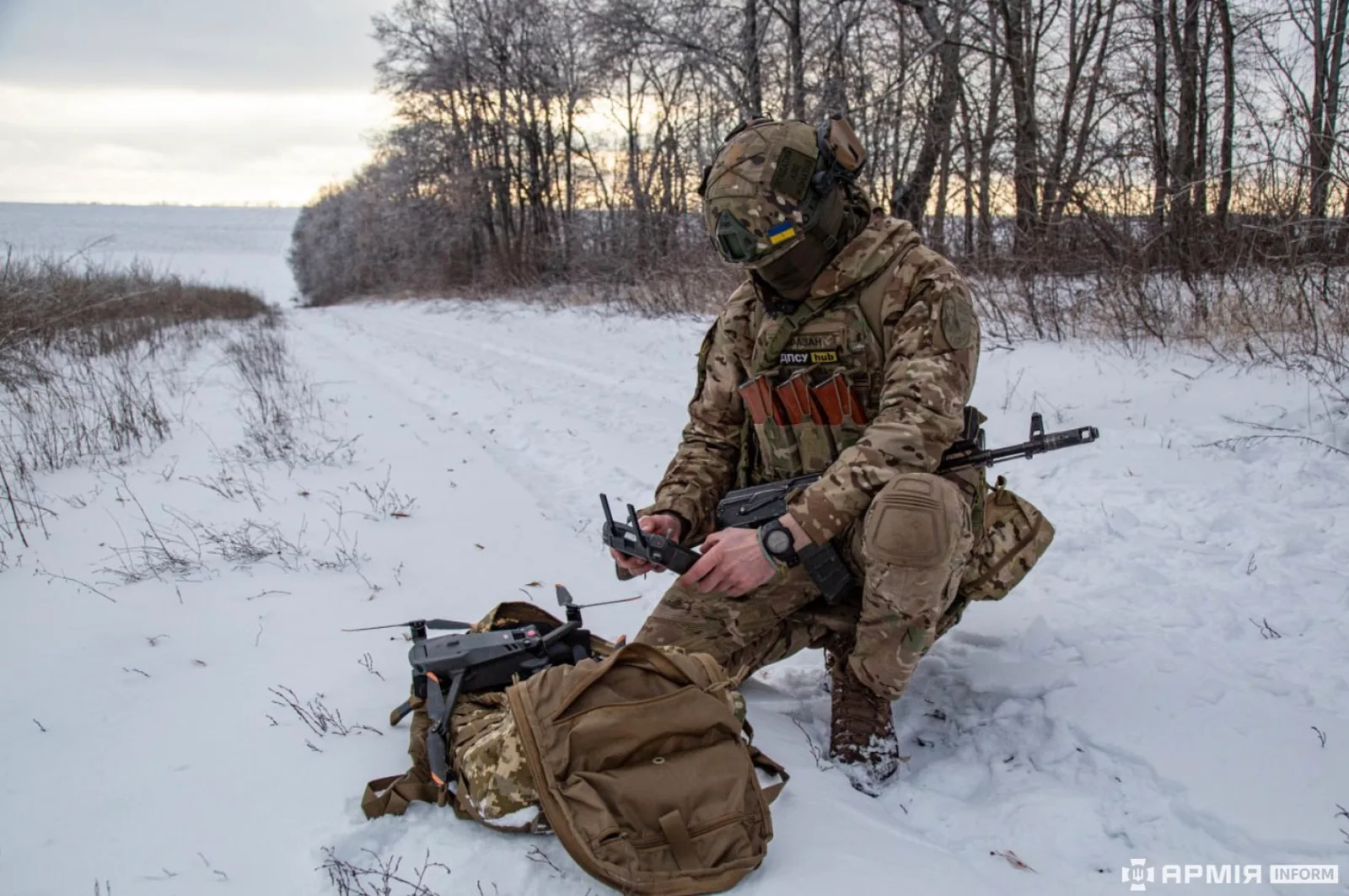 Ukrainian Border Guard soldier in winter camouflage kneeling in snow with a DJI Mavic drone and its controller