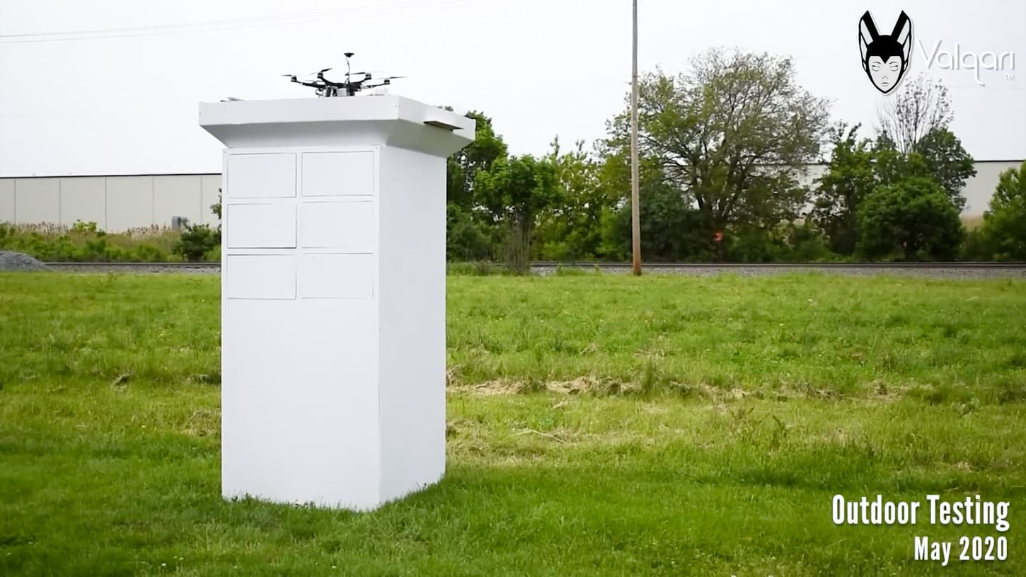 An early Valqari smart mailbox prototype under outdoor testing in a grass field in May 2020, with a drone perched on its landing platform