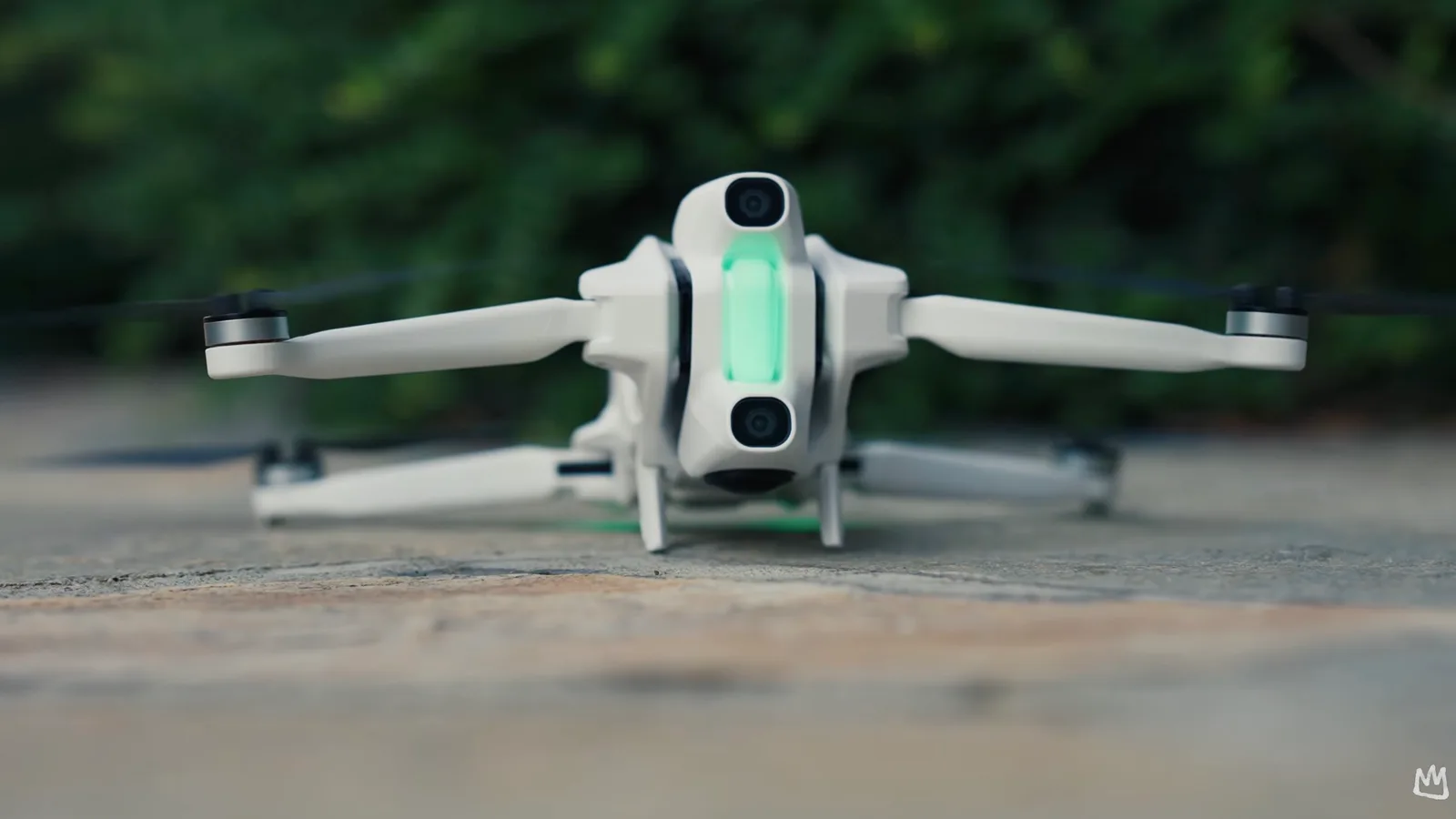 Rear view of a white compact folding camera drone resting on a stone surface with its green status light glowing