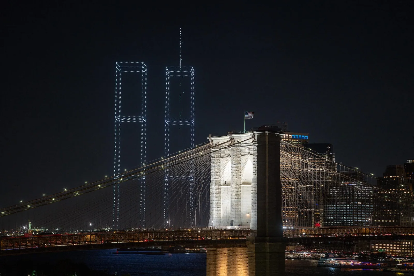 Drone light display recreating the Twin Towers behind the illuminated Brooklyn Bridge at night