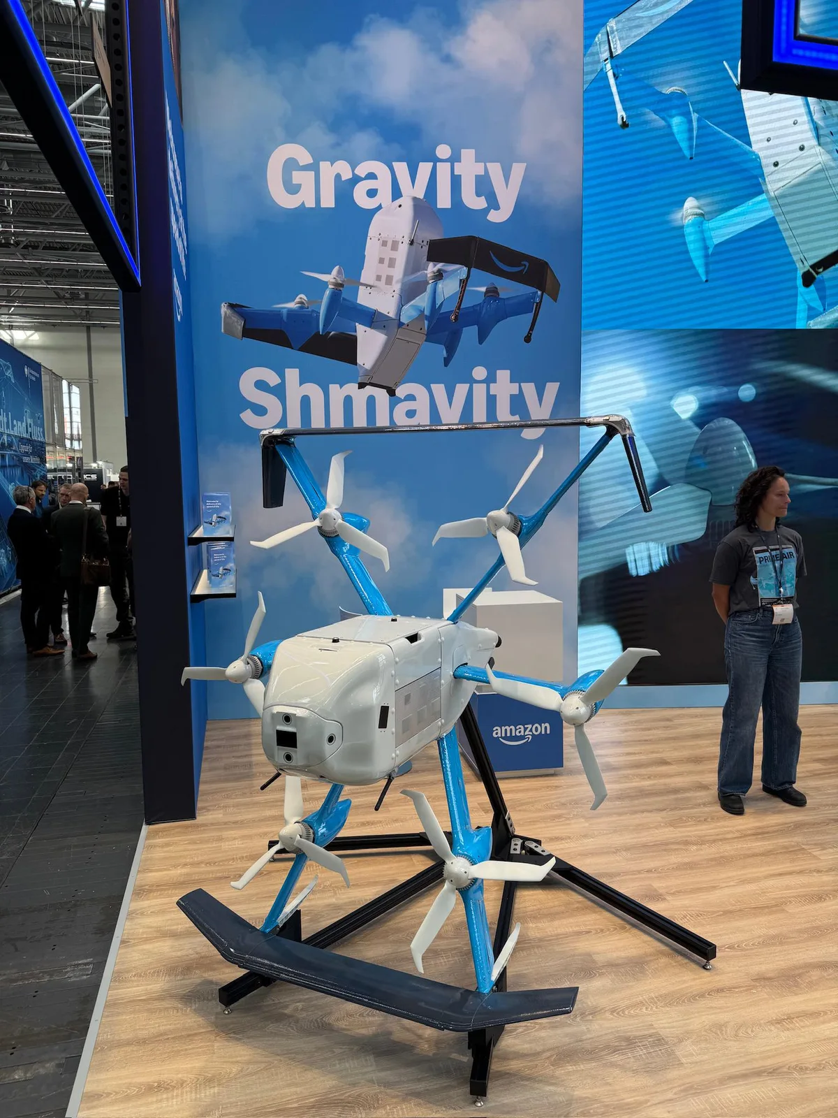 Amazon Prime Air MK30 delivery drone on a display stand in front of a blue Gravity Shmavity banner at a trade show booth in Dusseldorf
