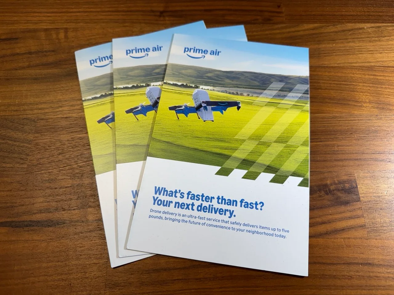 Three Amazon Prime Air drone delivery brochures fanned out on a wood table