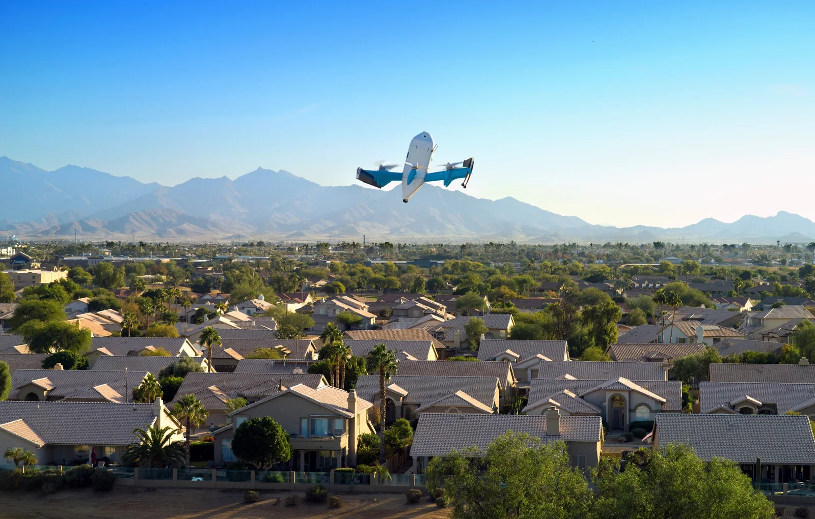 Amazon Prime Air MK30 delivery drone flying over a suburban neighborhood with mountains in the background