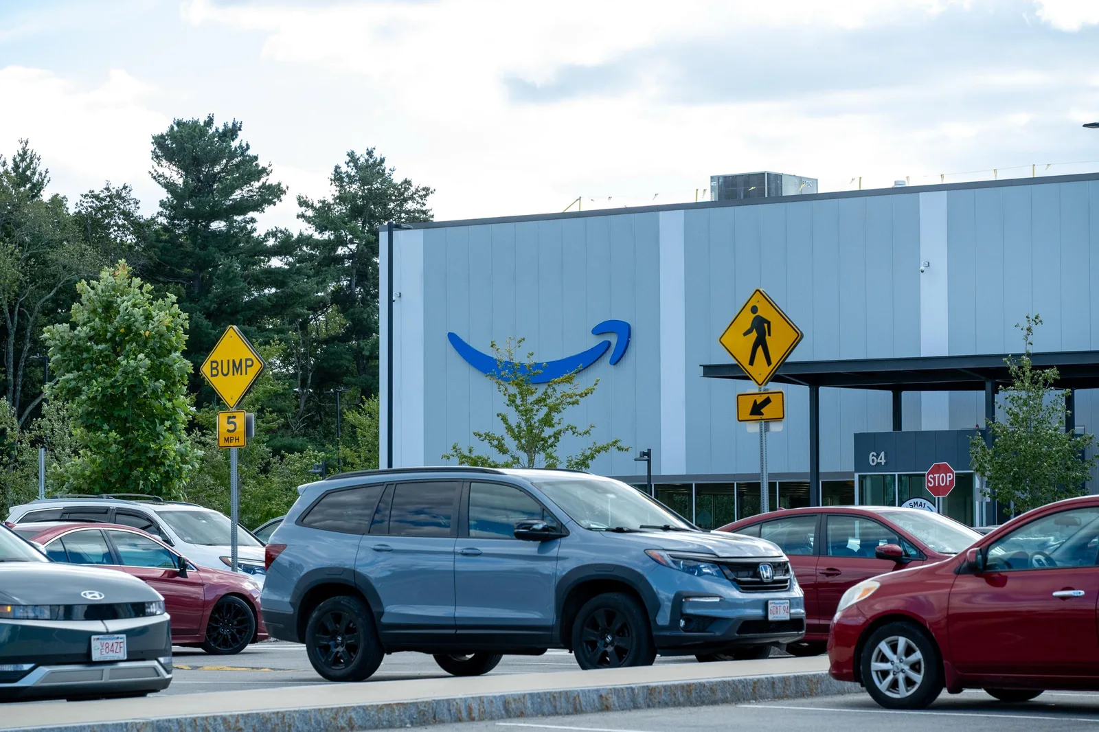 Amazon facility exterior with the Amazon smile logo and building number 64 in Westborough, Massachusetts, seen across a parking lot