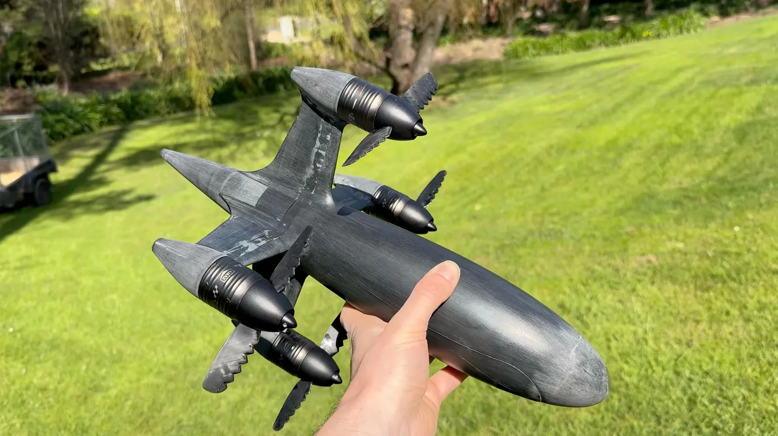 Benjamin Biggs holding his torpedo-shaped Blackbird speed drone with four propeller pods outdoors on grass