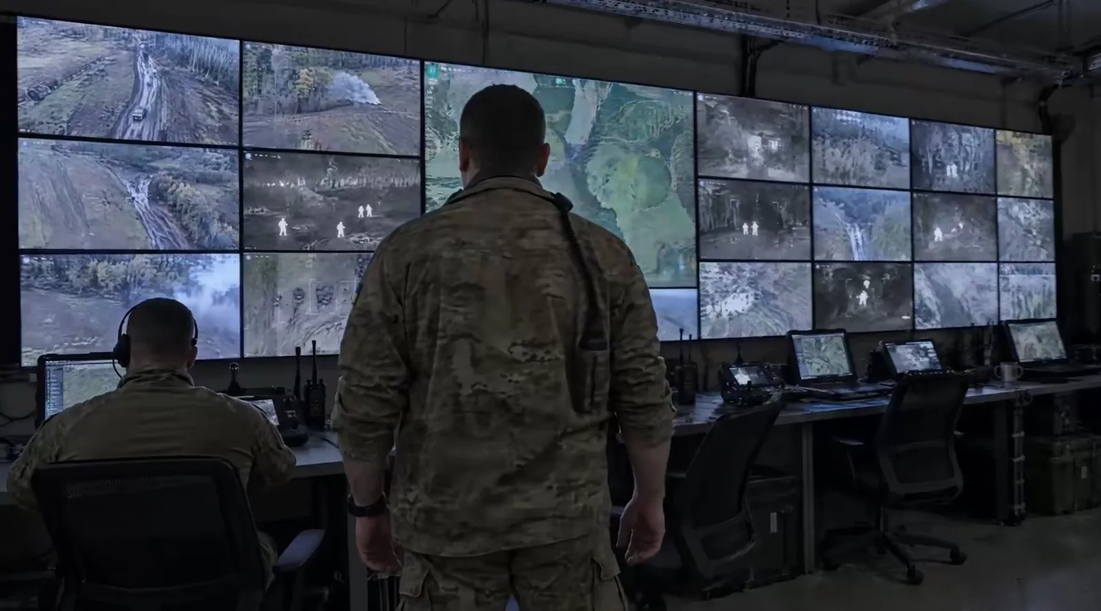 Ukrainian soldiers in a control room monitoring a wall of drone and thermal camera feeds
