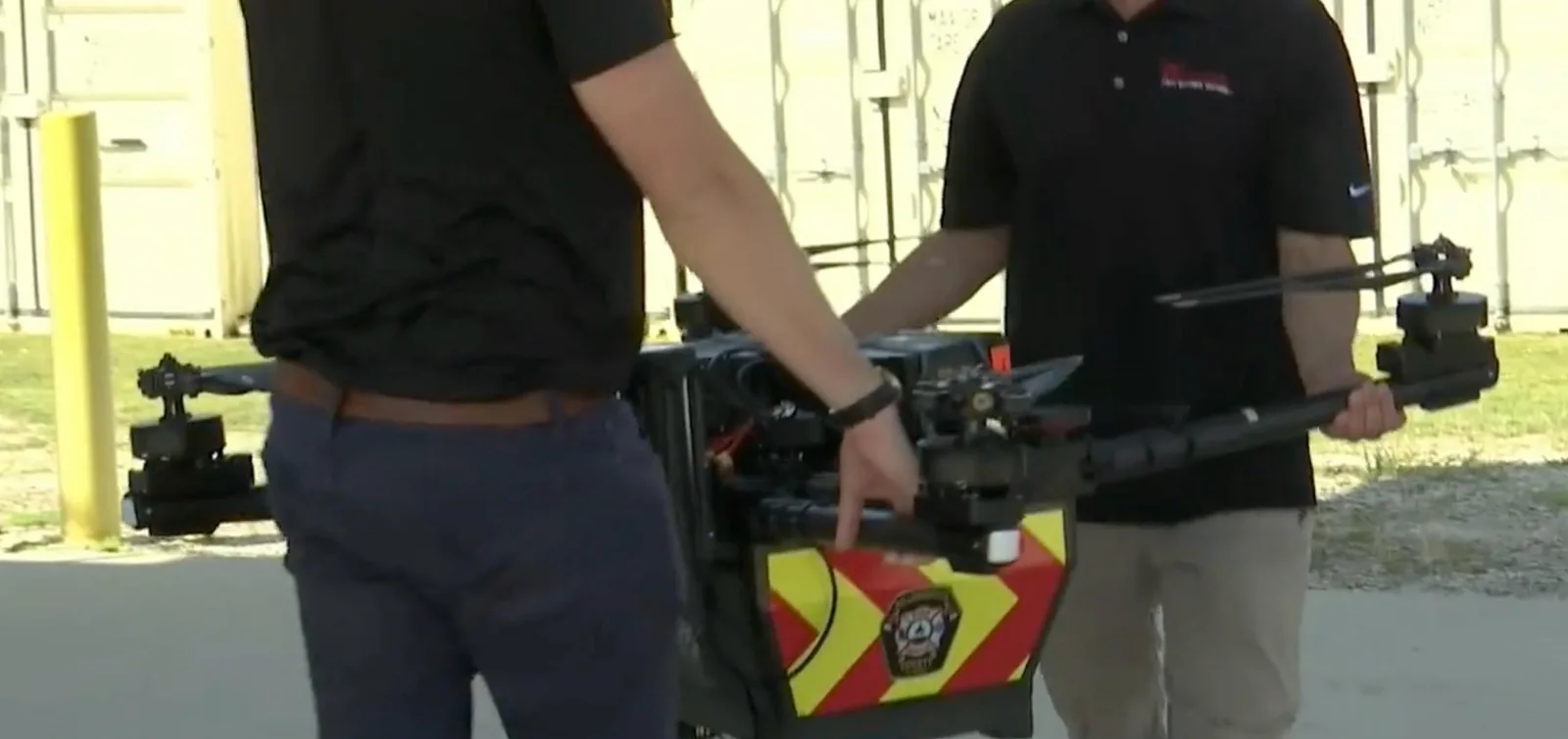 Two crew members carrying a large fire department rescue drone across pavement