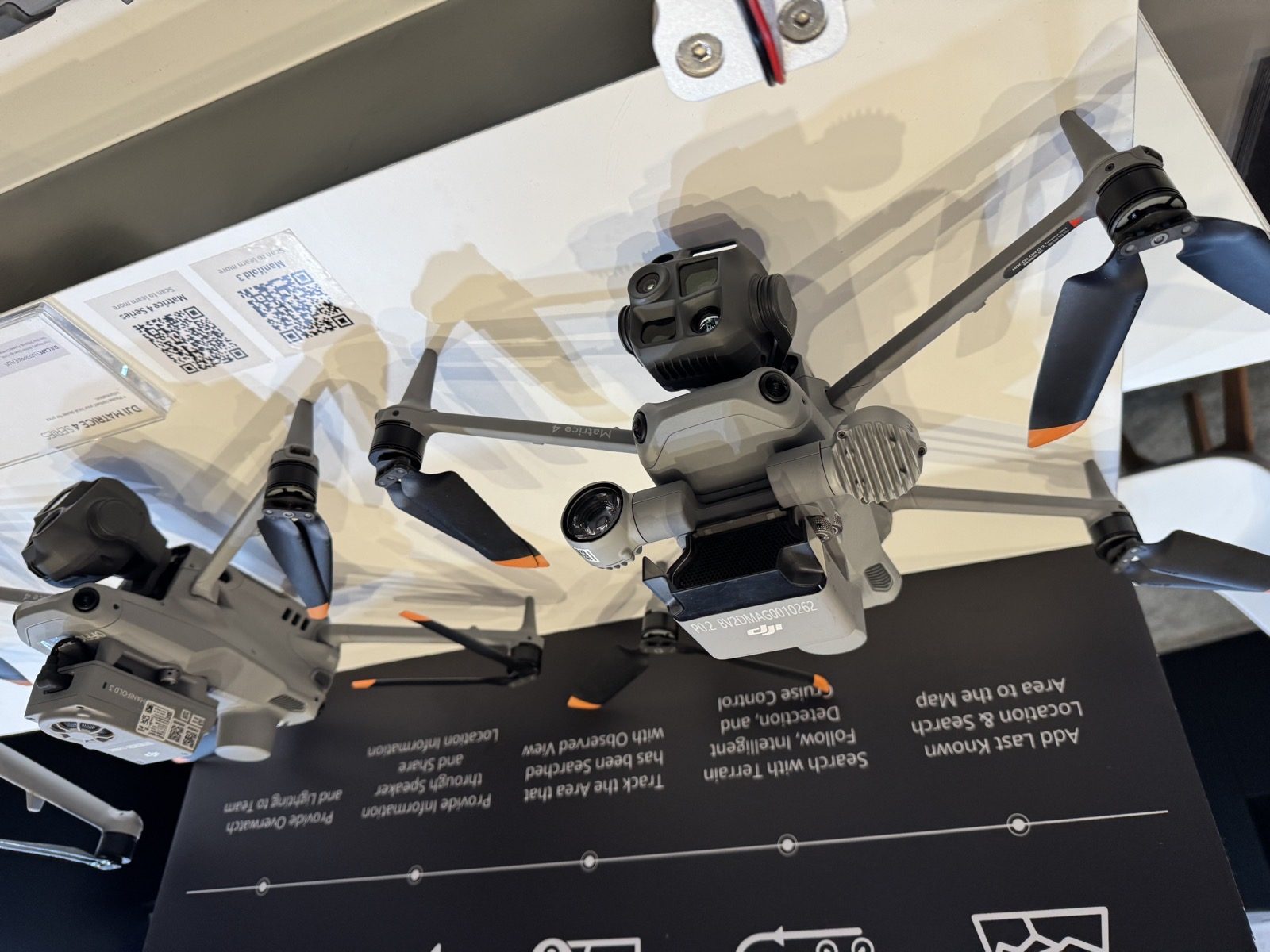 DJI Enterprise booth table at Commercial UAV Expo 2026 with a Matrice 400 carrying a Zenmuse P1, two Matrice 4 series aircraft, a Zenmuse L3 LiDAR on a stand and product brochures, with the FlightHub Analyzer slide on the screen behind