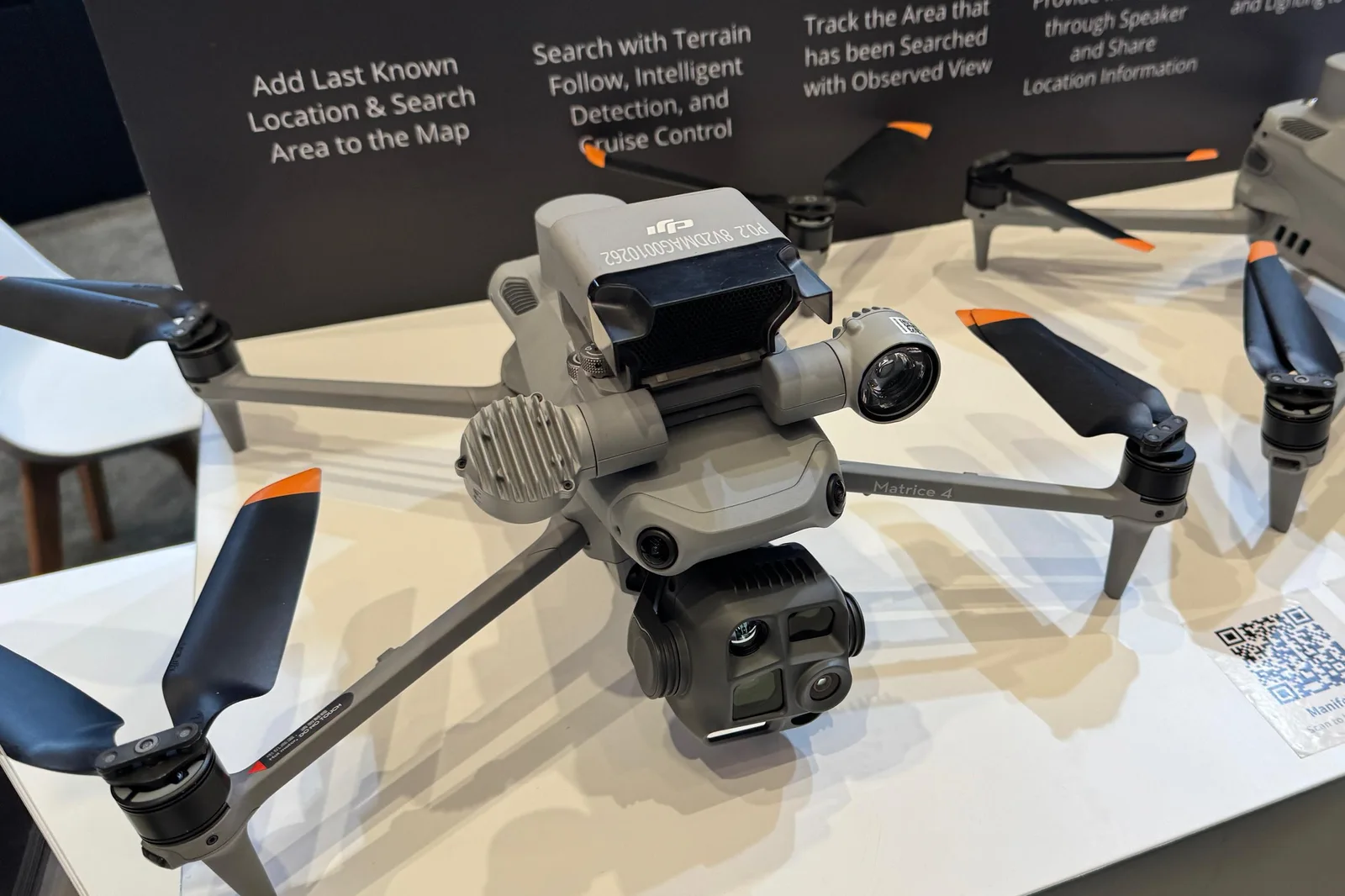 DJI Matrice 4T quadcopter on a white display table with its thermal and visual camera gimbal and top-mounted accessory, at DJI Enterprise Booth 903 at Commercial UAV Expo in Las Vegas.