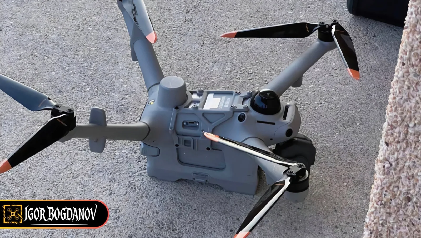Gray DJI Matrice 5TD prototype drone on asphalt with arms folded, a cylindrical antenna and dark dome on the top deck, and a multi-window gimbal
