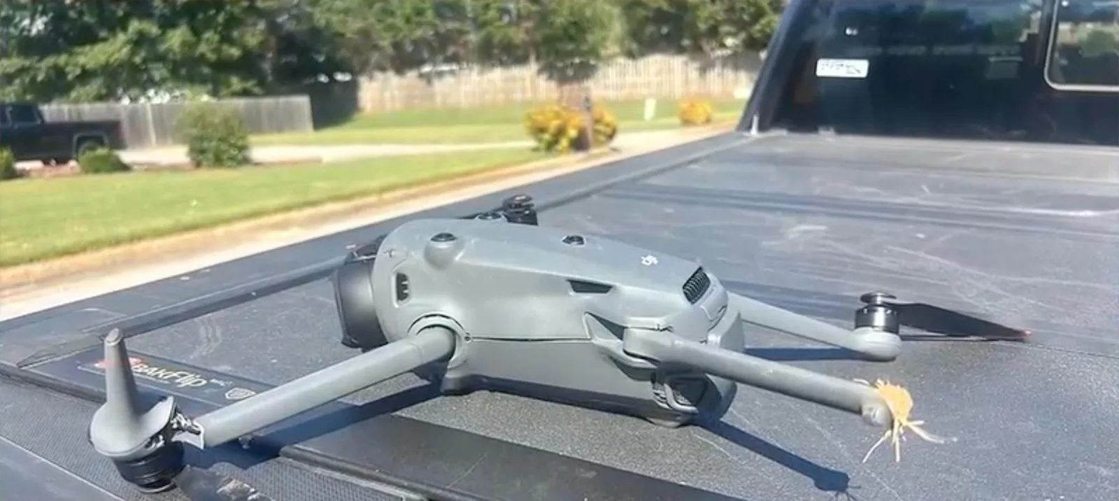 Damaged gray DJI Mavic 4 Pro drone resting on a black pickup truck bed cover, with a bent propeller arm and debris tangled in one motor