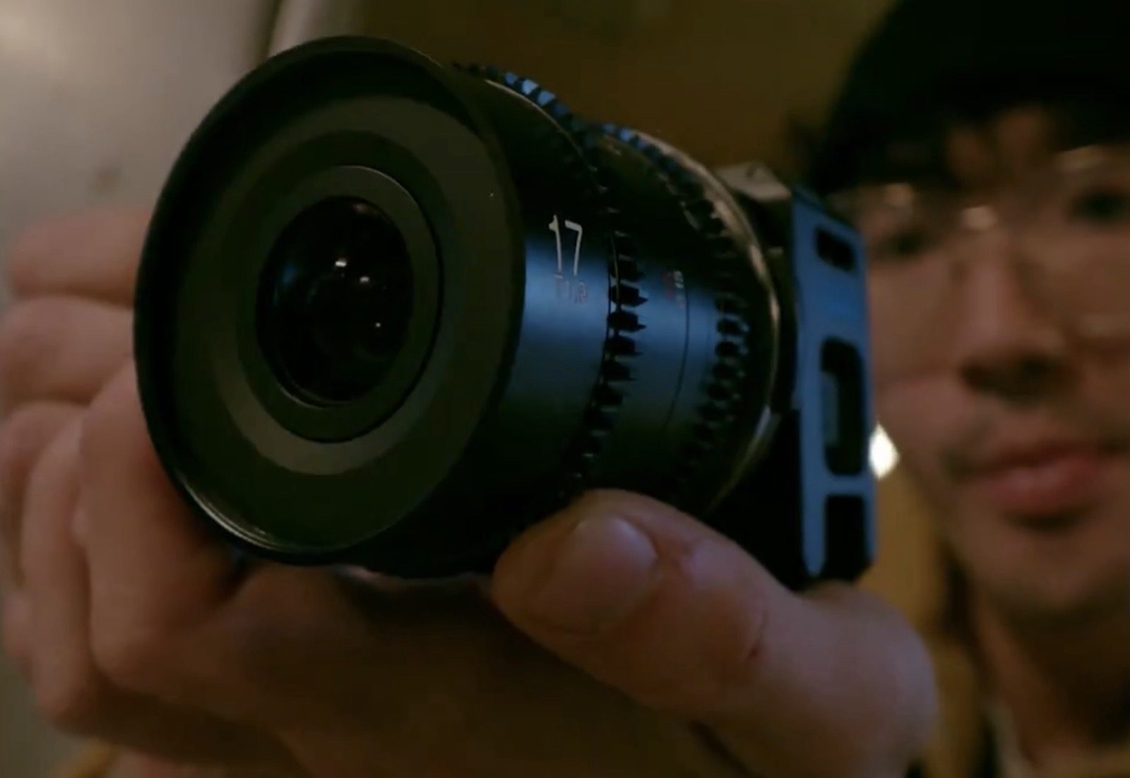 Close-up of two hands fitting a manual-focus Micro Four Thirds cine lens onto the GoPro MISSION 1 PRO ILS, with the aperture ring markings visible and the camera's front screen lit