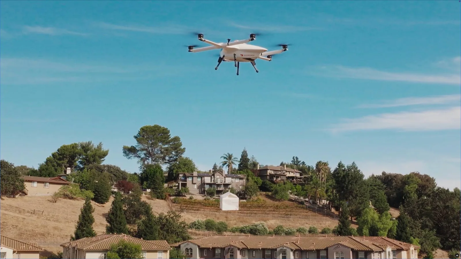 DoorDash Air delivery drone hovers over a residential hillside while lowering a package on its winch tether