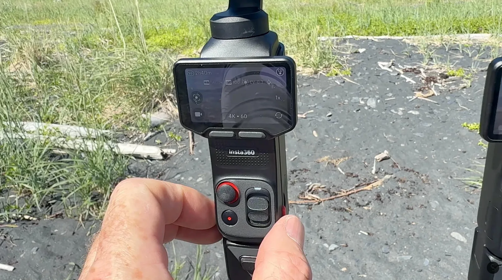 Hand holding the Insta360 Luna Pro camera outdoors, screen showing 4K 60 recording settings