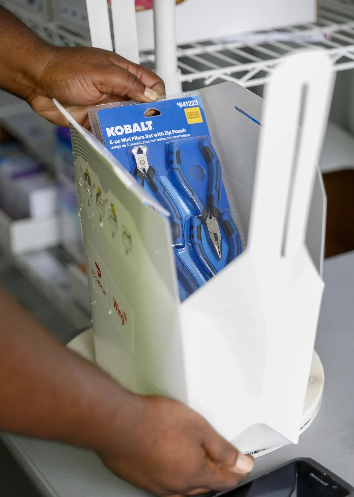 Hands placing a blue Kobalt six-piece mini pliers set into a white delivery box printed with the DoorDash and Wing logos