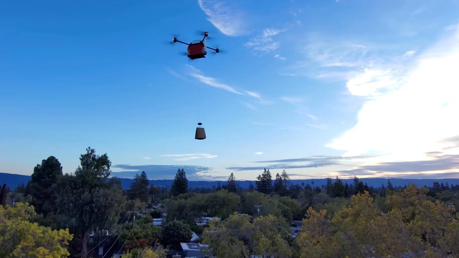 Matternet M3 delivery drone lowering a package on a cable over a suburban neighborhood