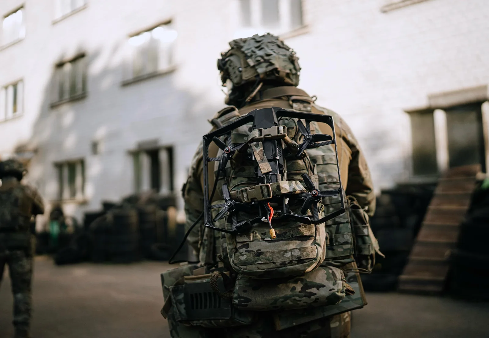 Soldier in multicam uniform seen from behind with a carbon-frame FPV drone strapped to their backpack