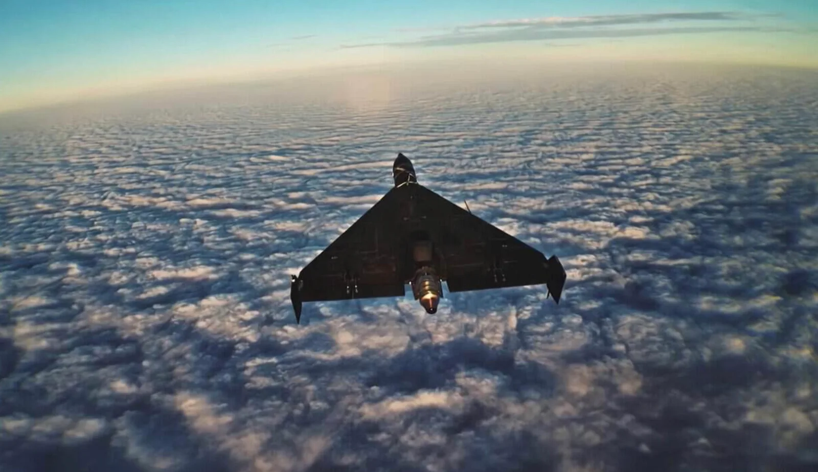 Rear view of a dark delta-wing jet drone with glowing engine exhaust flying above a cloud layer at sunset, still from SBU footage released September 19, 2026