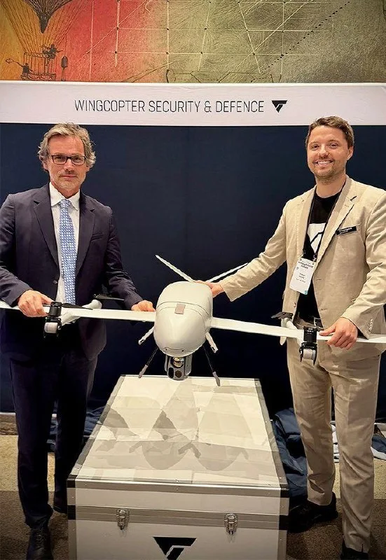 Two executives holding the Wingcopter 262 drone at a Wingcopter Security & Defence booth display