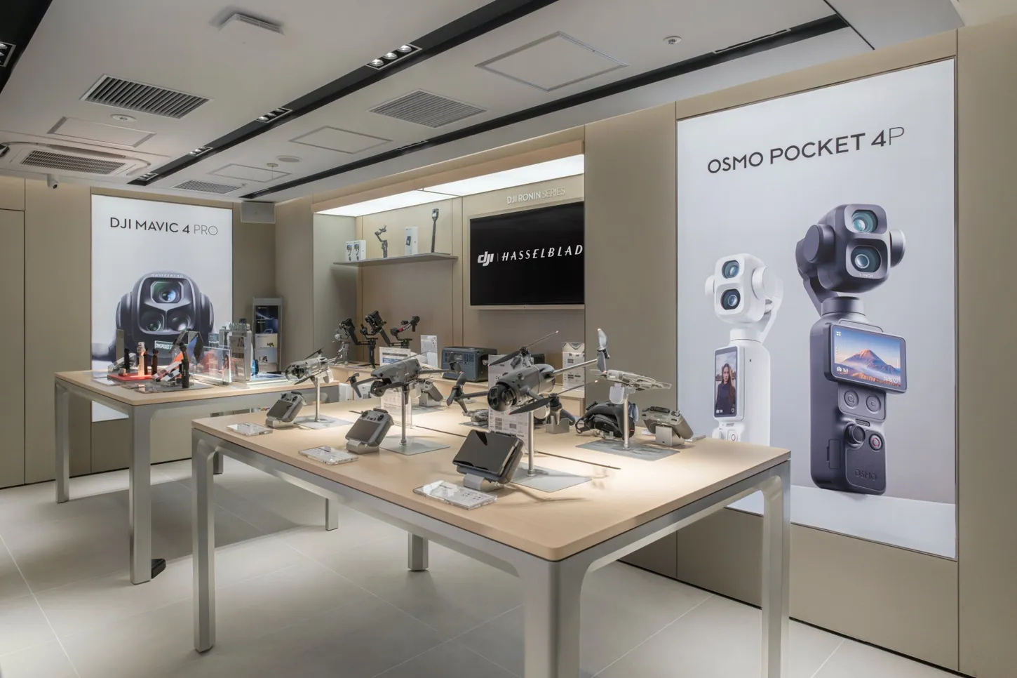 DJI drones, controllers and gimbals on wooden display tables, with a DJI Mavic 4 Pro poster on the left wall and an Osmo Pocket 4P poster on the right