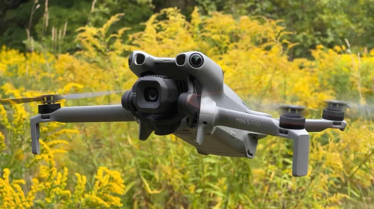 DJI Mini 5 Pro hovering head-on in front of blooming goldenrod, its forward LiDAR and vision sensors facing the camera