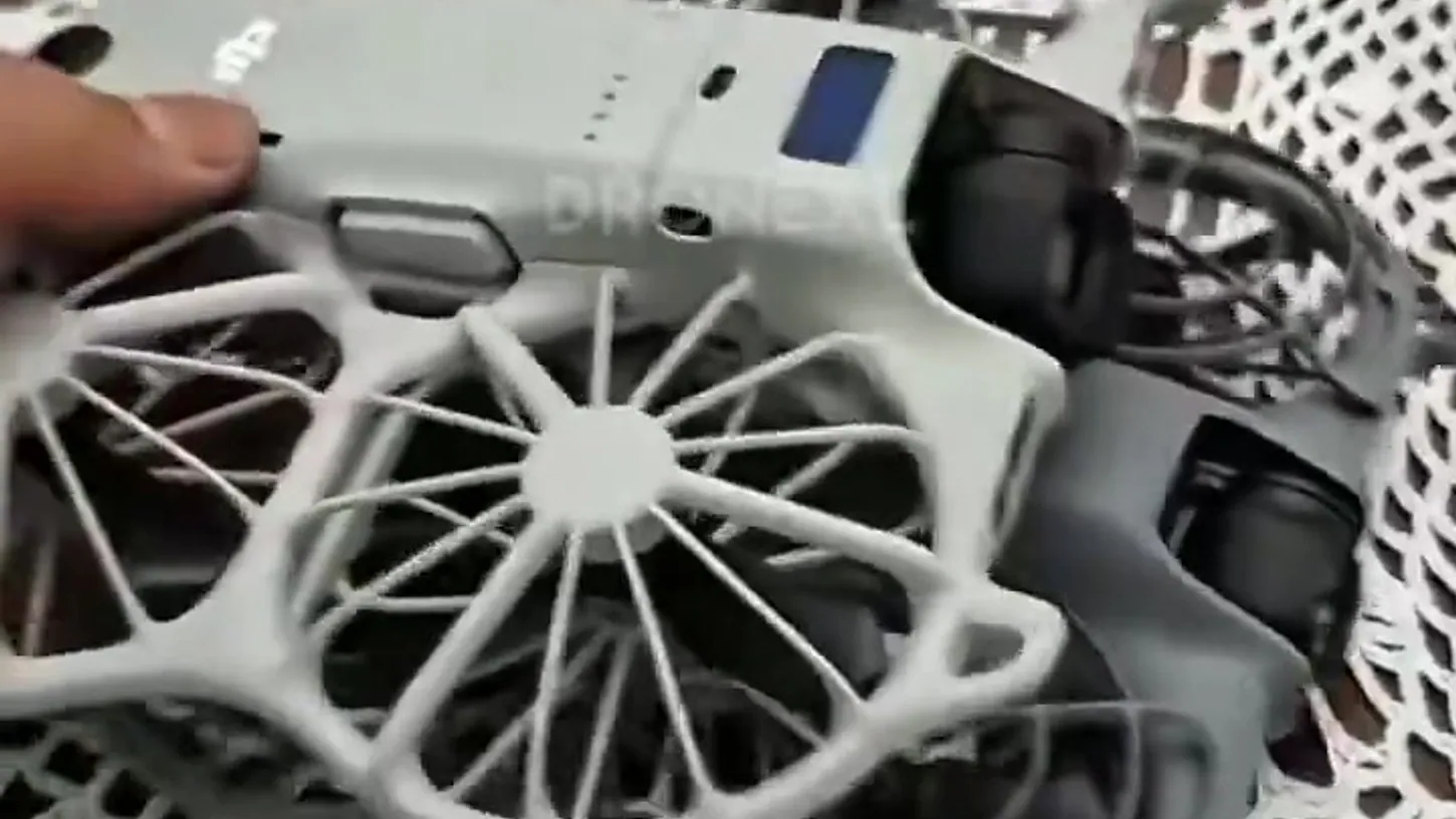 White DJI Neo 3 with spoked propeller cages resting on top of a smaller grey DJI Neo 2 on a lace tablecloth