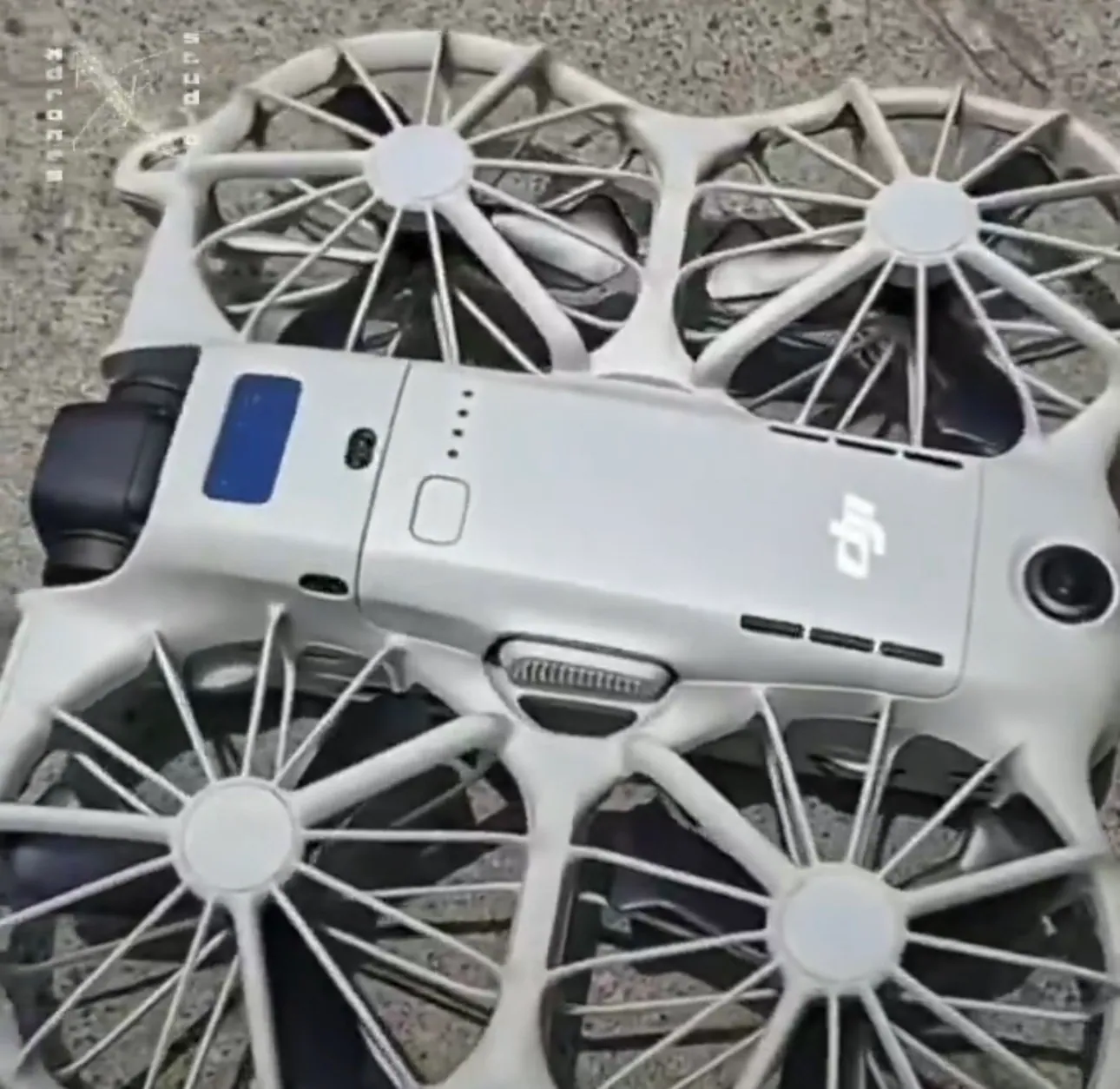 Top view of a white DJI Neo 3 on grey paving, showing a blue screen on the nose, four LEDs and a power button on the battery, a ribbed grille at the rear, a round sensor at the tail and vent slots along the side