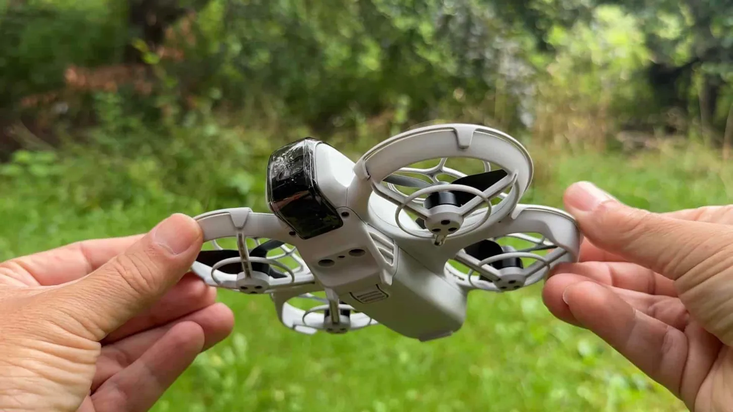 DJI Neo held in two hands, camera and gimbal protector facing the lens, propeller guards on