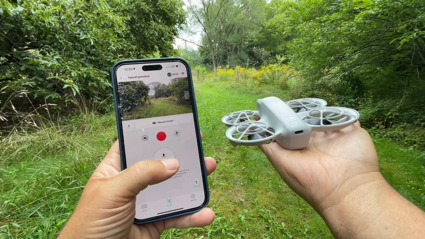 A pilot holds a phone running the DJI Fly app in one hand and the DJI Neo on the other palm, ready for takeoff