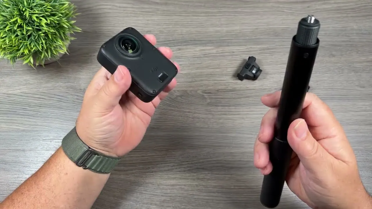 Shawn holding the DJI Osmo 360 II in one hand and a black extension pole with a quarter-inch screw in the other, with a magnetic mount on the table between them.