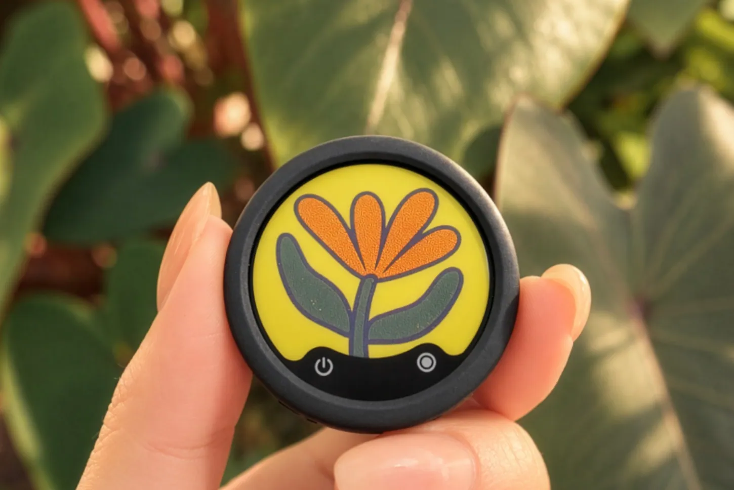 A hand holds a round Insta360 Mic transmitter whose E-Ink screen shows an orange flower on a yellow background, with power and record icons at the bottom.