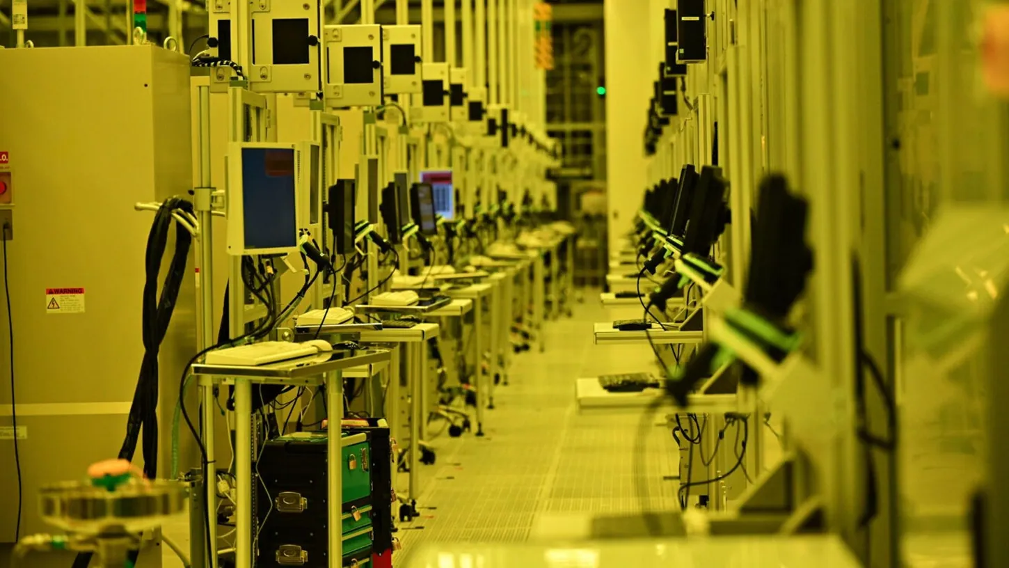 Rows of semiconductor manufacturing tools and monitors under yellow light inside an Intel cleanroom