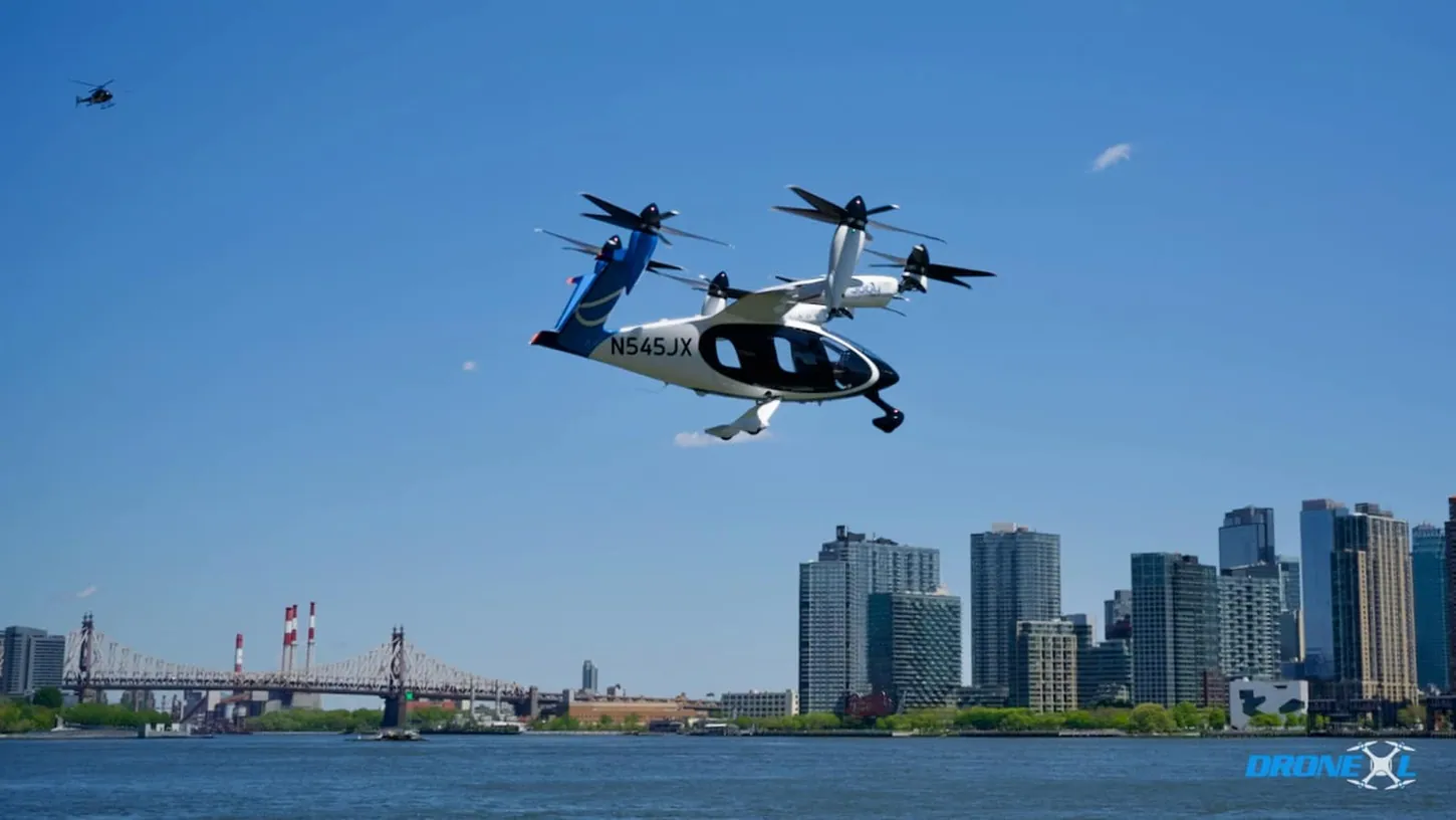 Joby air taxi N545JX flying over the East River with the Queensboro Bridge and Long Island City skyline behind it