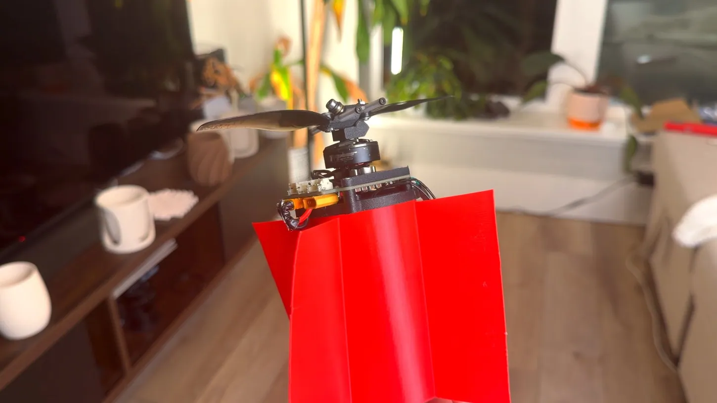 Red 3D printed drone body with anti-torque vanes topped by a single motor and a two-blade hinged propeller hub