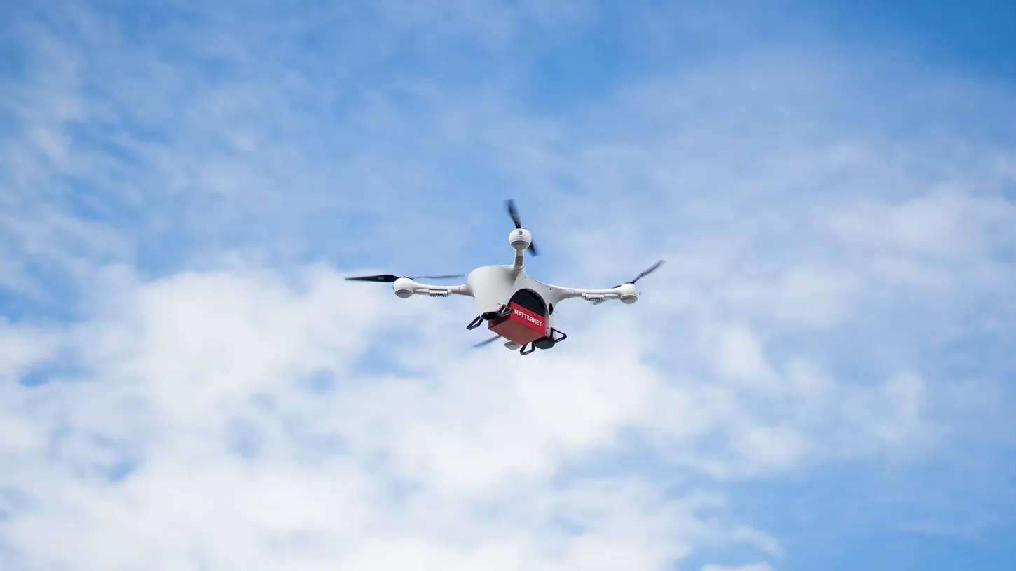 Matternet M2 delivery drone flying against a blue sky with a red Matternet cargo box under its body