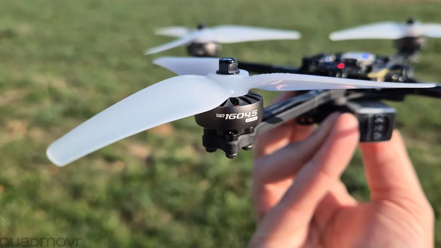 Close-up of a black ITS 1604.5 brushless motor with a white tri-blade propeller on a carbon drone arm held in a hand