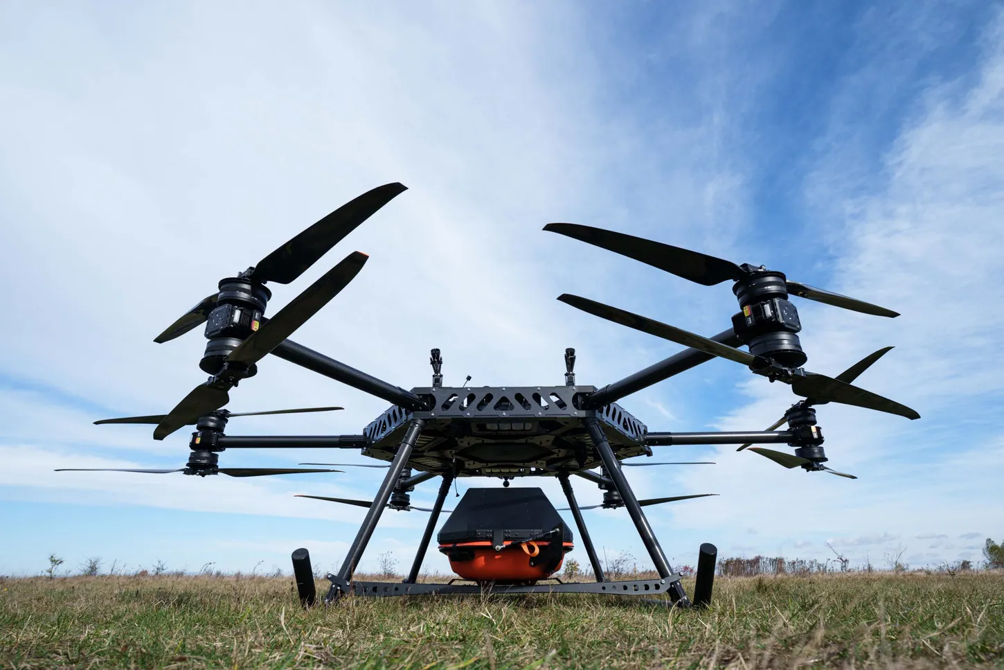 StarGate drone parked on grass, seen from a low angle, with six folding arms and an enclosed orange stretcher pod under the center frame