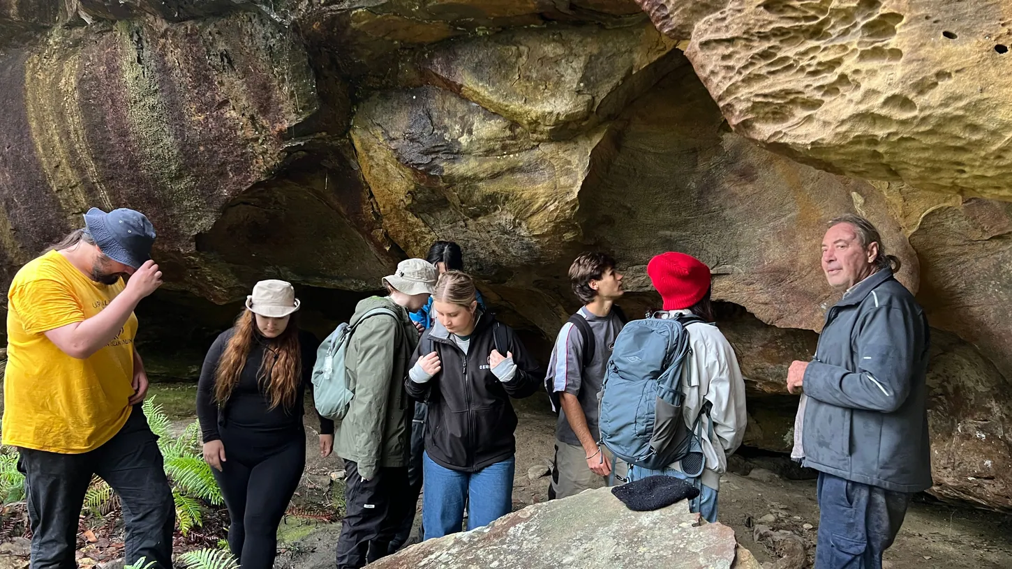 Wayne Brennan stands with a group of students under a large sandstone overhang in the Blue Mountains