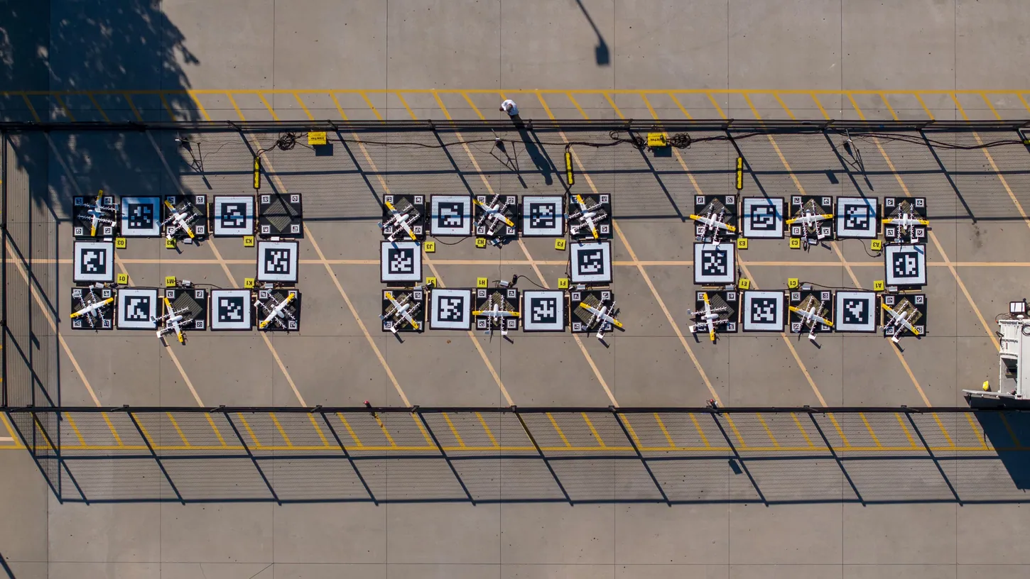 Aerial view of three groups of six Wing drone landing pads with aircraft parked on them, marked with black and white fiducial squares