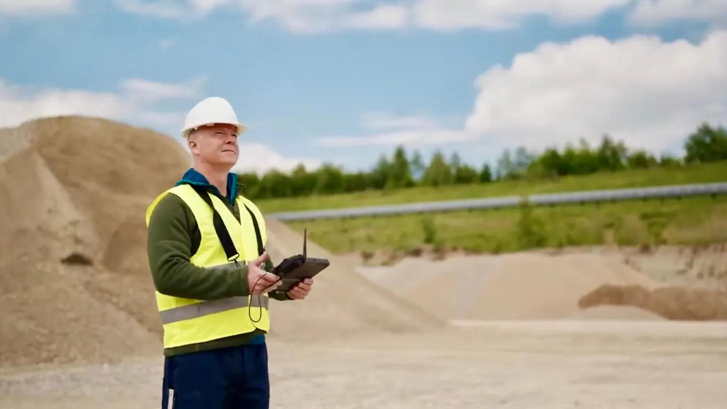 Operator in a white hard hat and yellow hi-vis vest holding a tablet controller at a gravel quarry