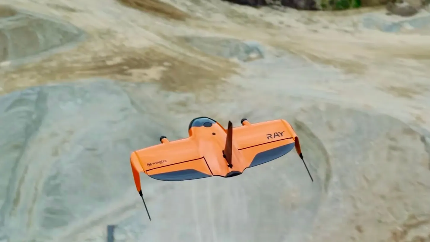 Top view of the orange WingtraRAY flying wing with its vertical fin, seen from above over bare quarry ground