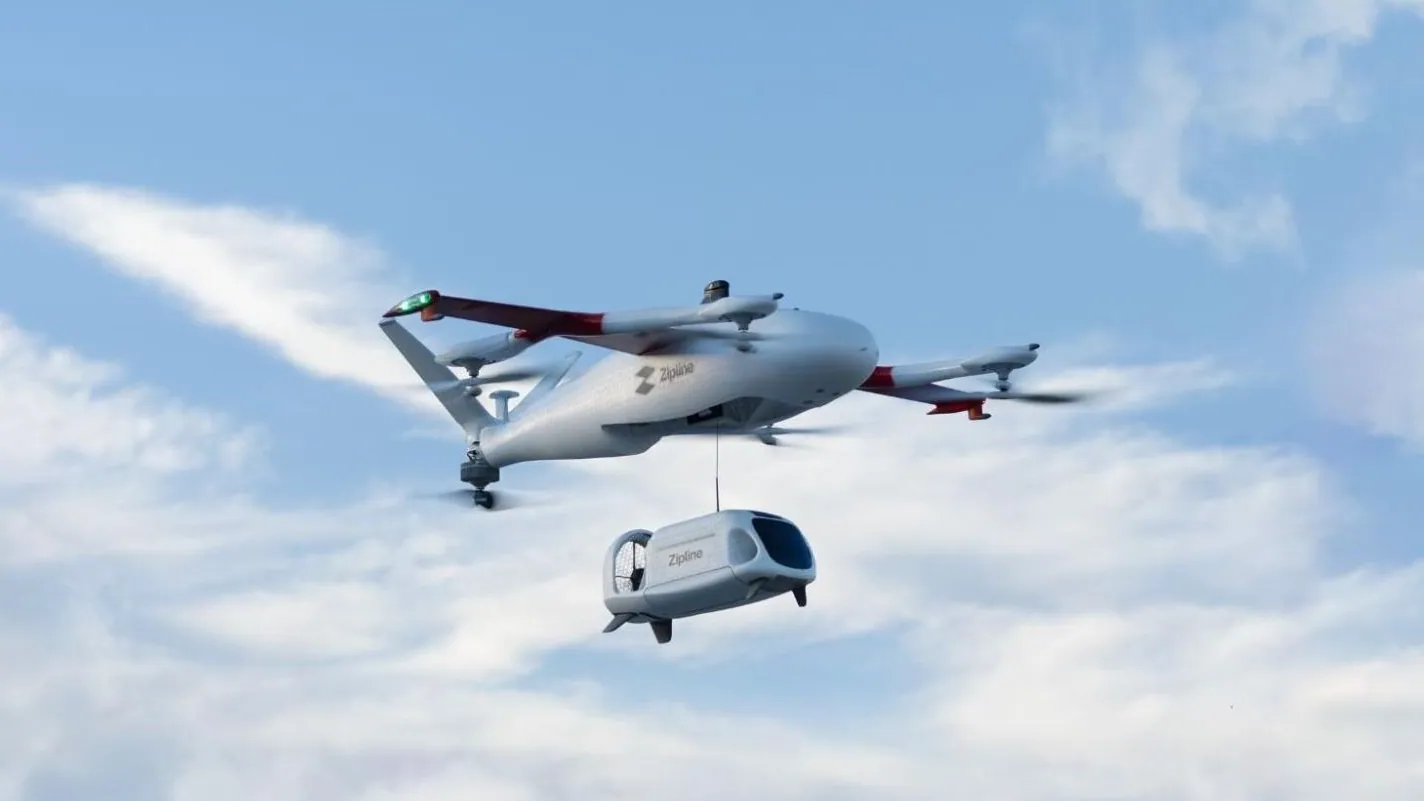 White Zipline Platform 2 delivery drone hovering against a blue sky with its delivery droid hanging below it on a tether