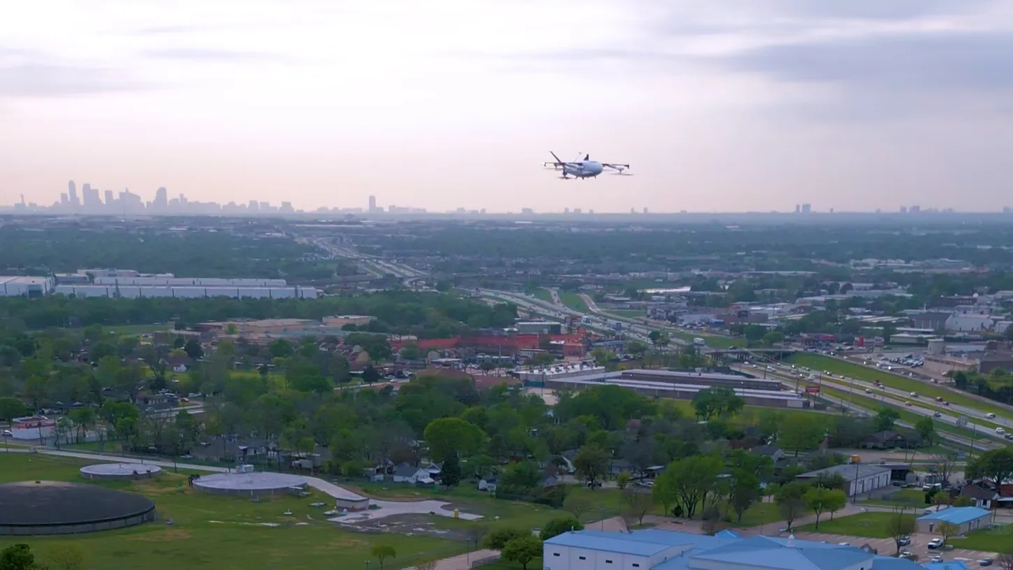 Zipline Platform 2 delivery drone flying over a Texas suburb with highways, warehouses and a downtown skyline on the horizon